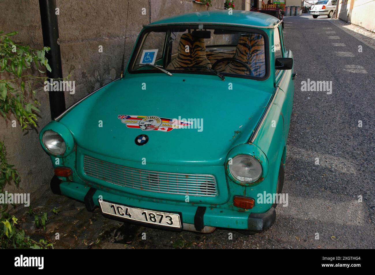 Rostgrüner Trabant mit Tigerfell-Kunstbezug, 2006 auf einer Straße in Tábor, Südböhmen, Tschechien. Der Trabant, der 1957 auf den Markt kam, wird manchmal als „das schlechteste Auto aller Zeiten“ bezeichnet. Mit dem Fall der Berliner Mauer wurde es 1989 zu einem Kultfahrzeug in Deutschland. Dieser Trabant hat ein BMW-Logo und einen Aufkleber mit dem Aufdruck „International Truck Driver“ auf der Motorhaube oder der Motorhaube sowie einen Parkschein für Behinderte in der Windschutzscheibe. Stockfoto