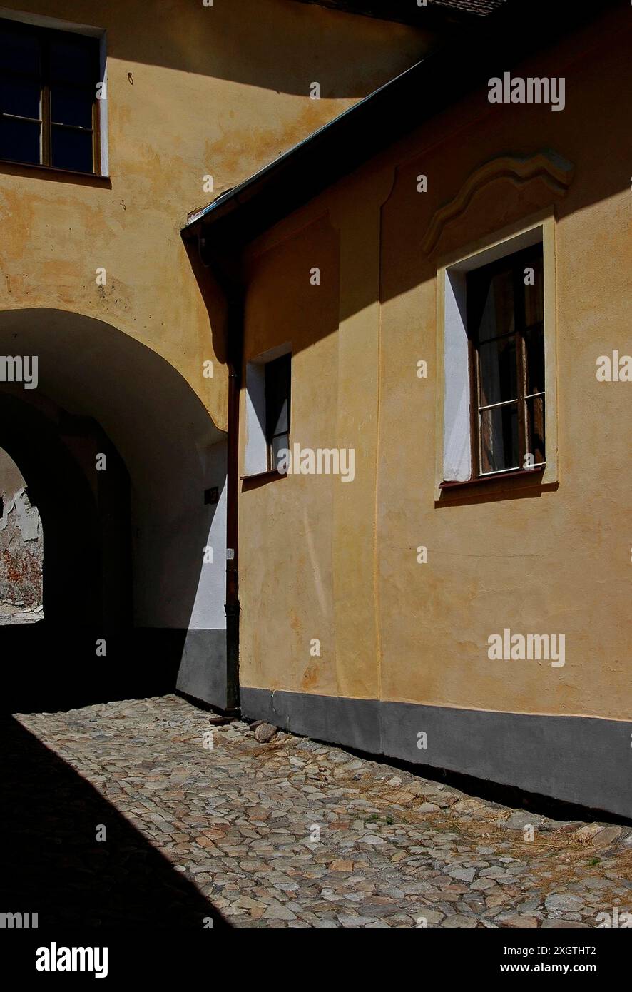 Sonnenlicht erwärmt die ockergetünchte Südwestwand eines antiken Bogens in Tábor, Südböhmen, Tschechien. Der Bogen erstreckt sich über Martínka Húsky, eine gepflasterte Gasse, die von der südwestlichen Ecke von Žižkovo Námestí, dem großen zentralen Platz im historischen Herzen von Tábor, führt. Stockfoto