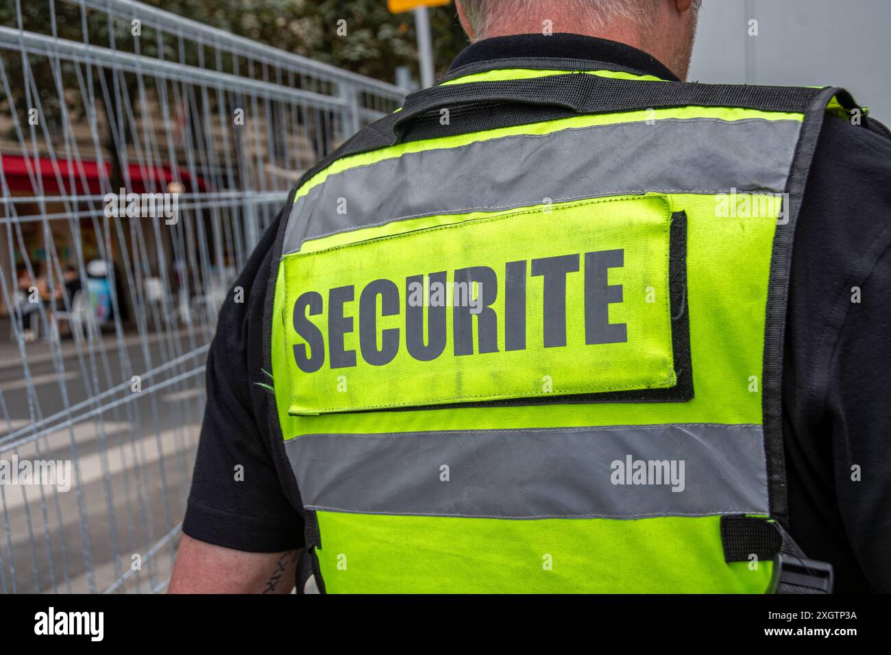 Fluoreszierende gelbe Weste mit dem Wort „Security“ auf der Rückseite, die von einem privaten Sicherheitsbeamten getragen wird, der einen sicheren Ort beobachtet Stockfoto