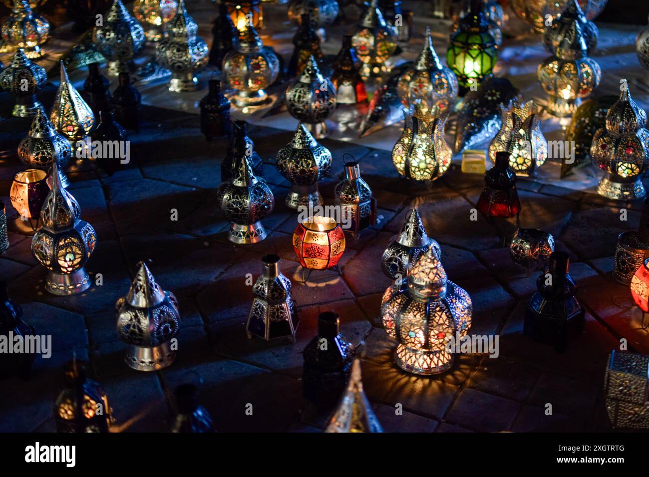 Eine beeindruckende Auswahl marokkanischer Laternen, die unter dem Nachthimmel in Marrakesch beleuchtet werden, mit komplizierten Metallarbeiten und lebendigen Glaspaneelen. Stockfoto