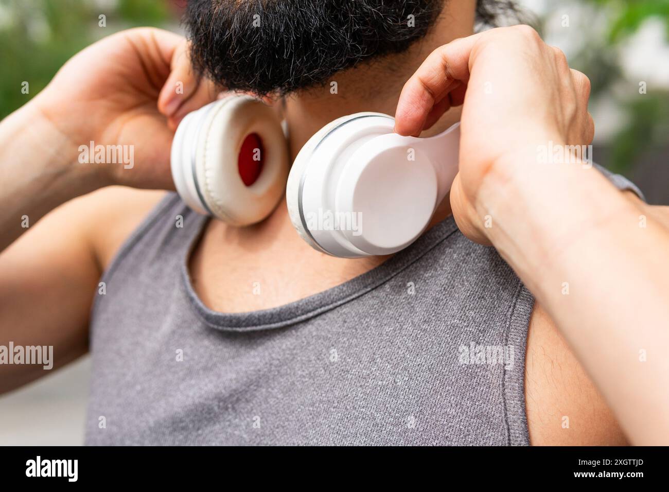 Nahaufnahme eines anonymen Mannes, der seine weißen Kopfhörer vor einem Workout in einem Stadtpark anpasst und sich auf eine sportliche und aktive Lifestyle-Session vorbereitet Stockfoto