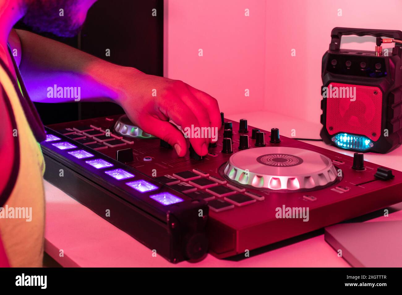 DJ stellt die Knöpfe und Schieberegler auf einer Mischkonsole unter leuchtendem Pink- und violettem Licht ein Stockfoto