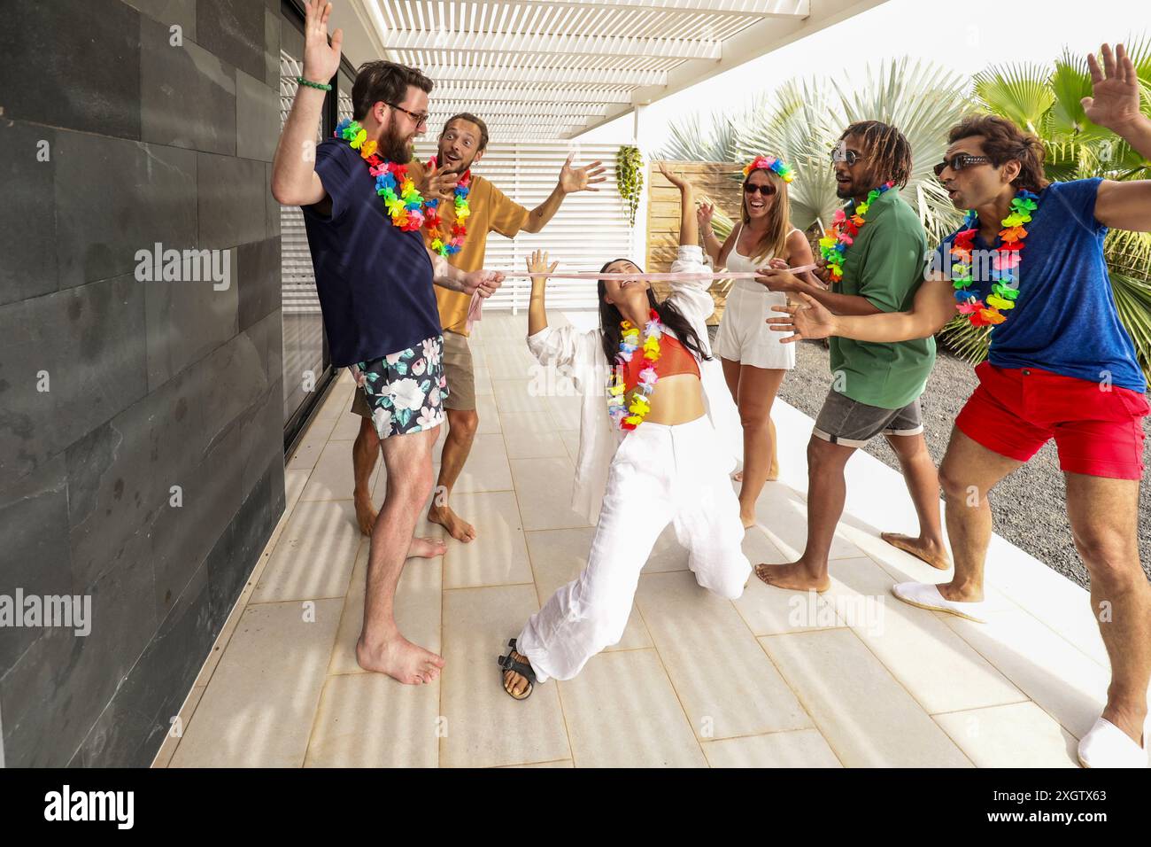 Eine dynamische Gruppe von Freunden tanzt fröhlich auf einer Sommerparty in der Nähe des Pools, mit lässigen Shorts und Blumenleis, die eine festliche tropische Atmosphäre hervorrufen. Stockfoto