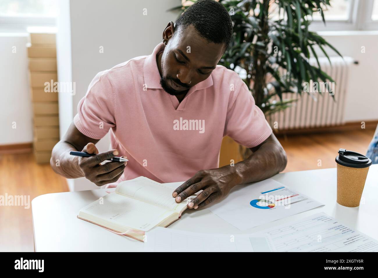 Ein afroamerikanischer Mann untersucht Dokumente in einem gut beleuchteten Coworking Space und zeigt organisierte Arbeiten mit Karten und einer Kaffeetasse in der Nähe. Stockfoto