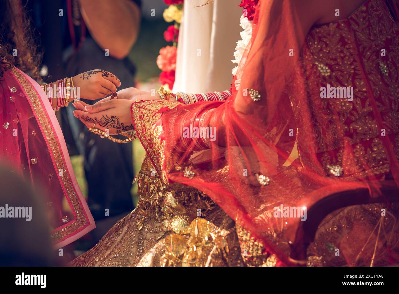 Traditionelle indische Brautkleider und Henna-verzierte, nicht erkennbare Frauenhände während einer Hochzeitszeremonie, die sich auf komplizierte kulturelle Deta konzentriert Stockfoto