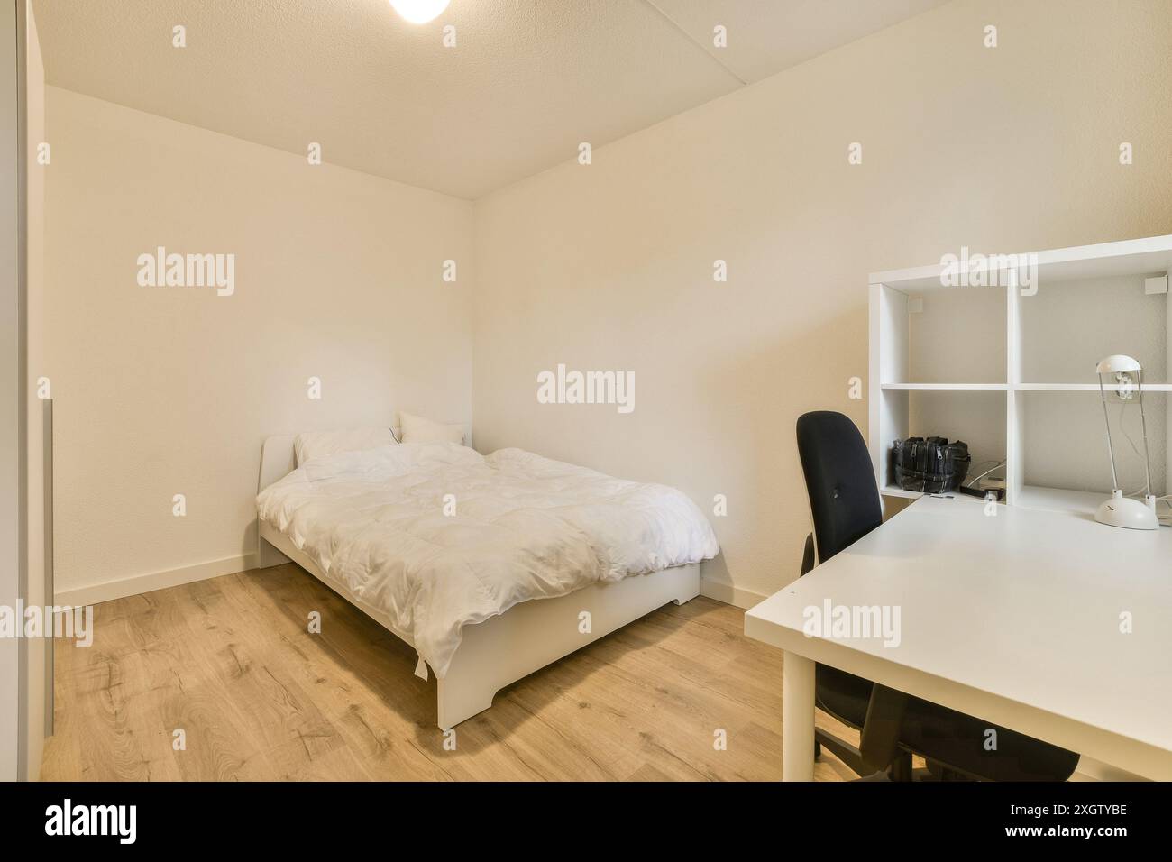 Ein ordentlich organisiertes minimalistisches Schlafzimmer mit einem weißen Bett und einem verbundenen Arbeitsbereich mit Schreibtisch, Stuhl und Regal in Henkenshage, Amsterdam Stockfoto