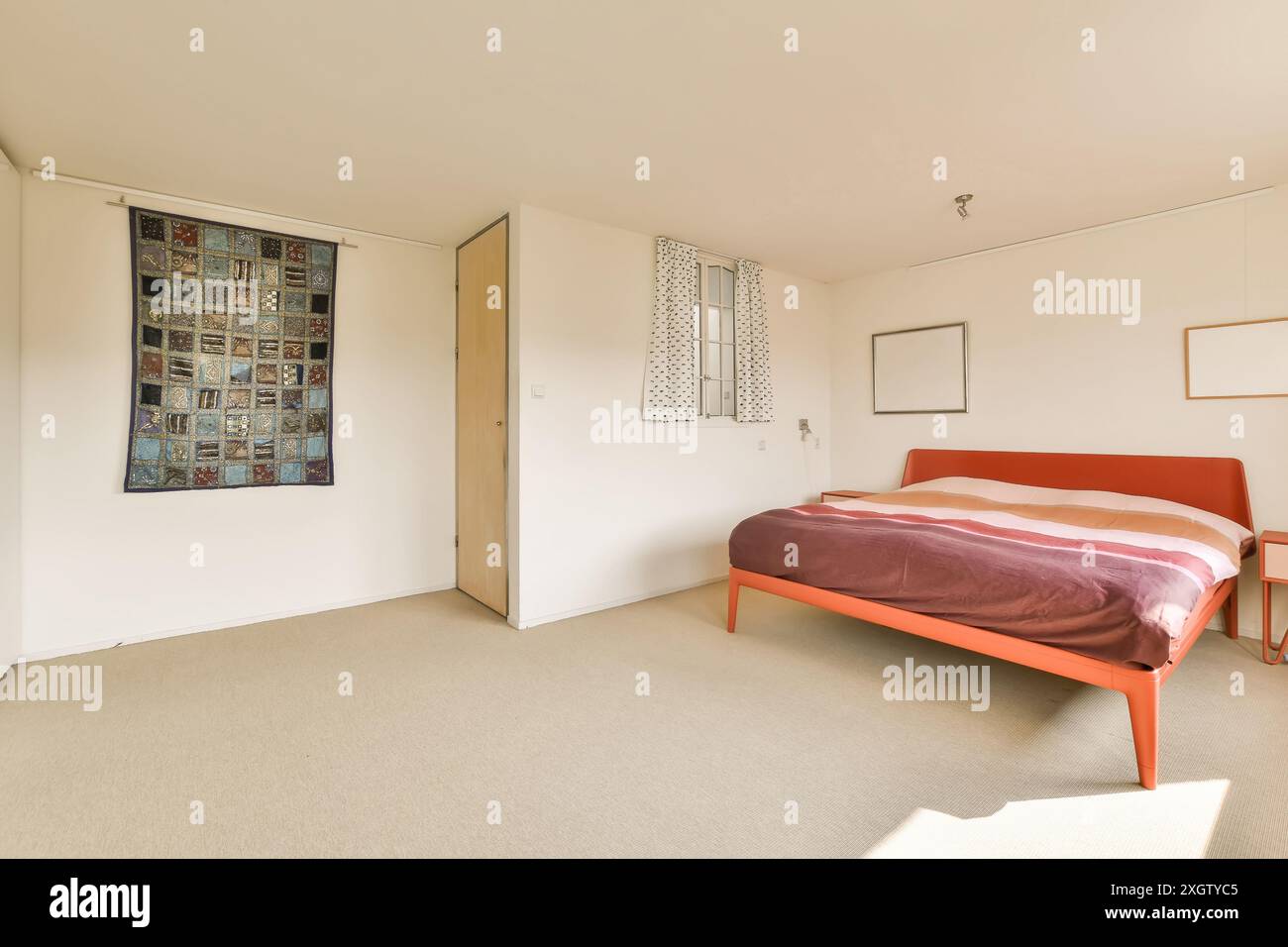 Geräumiges, sonnendurchflutetes Schlafzimmer mit minimalistischem Design, orangefarbenem Bettgestell, gestreiftem Bettlaken und bescheidenem Dekor Stockfoto
