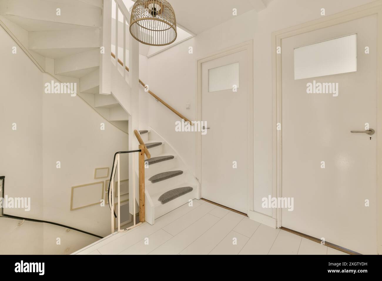Ein minimalistischer Hauseingang mit einer weißen Treppe mit Teppichboden, moderner Beleuchtung und eleganten Türen. Stockfoto
