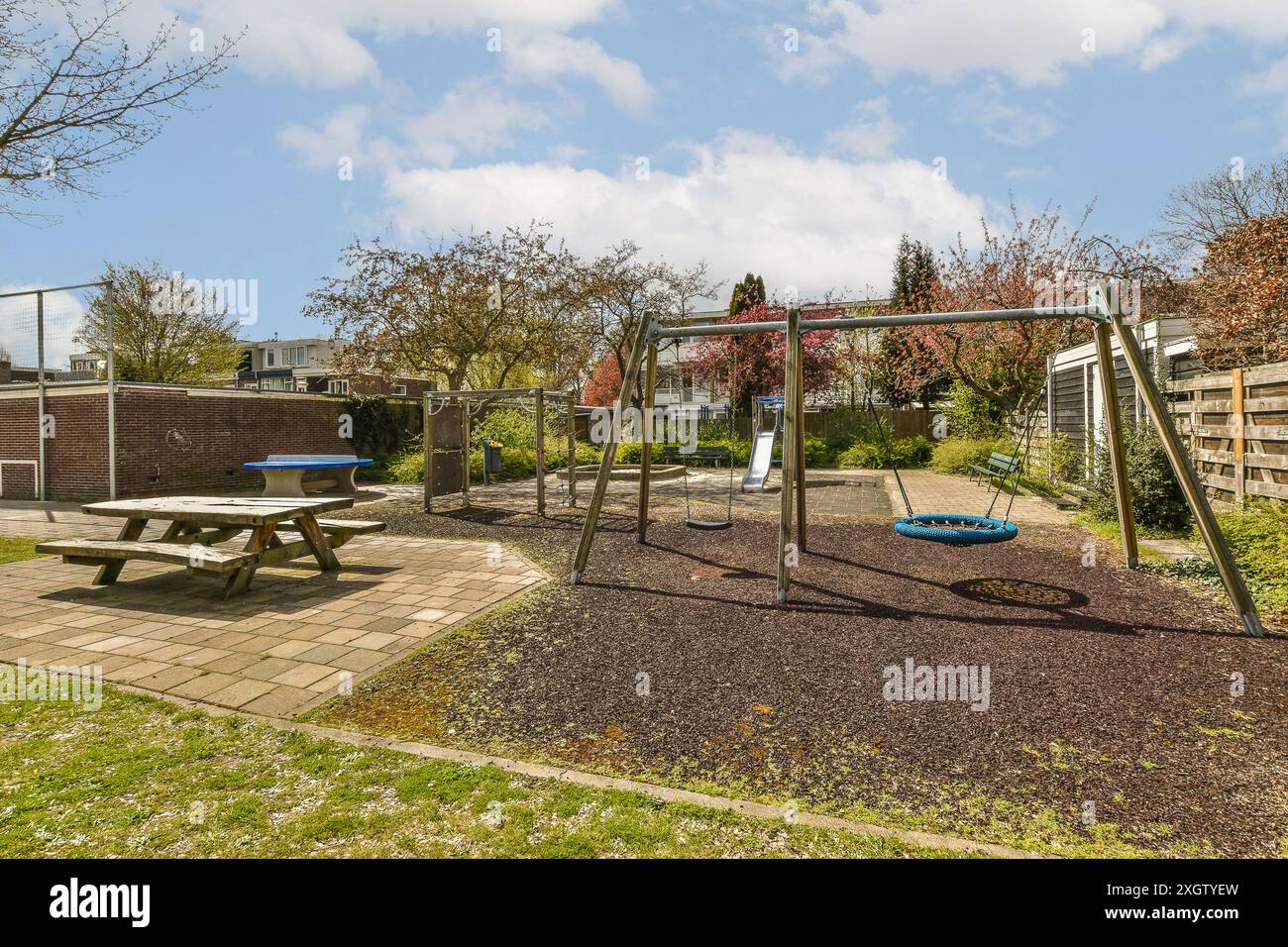 Ein gepflegter Spielplatz mit Schaukel, Rutsche und Picknicktisch unter klarem blauen Himmel bietet einen angenehmen Erholungsbereich im Freien. Stockfoto