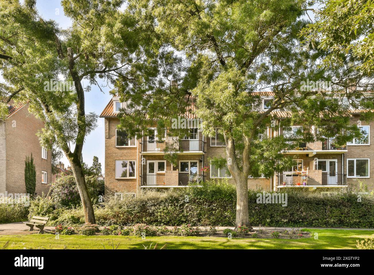 Ein vorstädtisches Ziegelhaus zwischen üppigen Bäumen, mit einem gepflegten Garten und einer einladenden Bank, die ein friedliches Wohnen veranschaulicht. Stockfoto