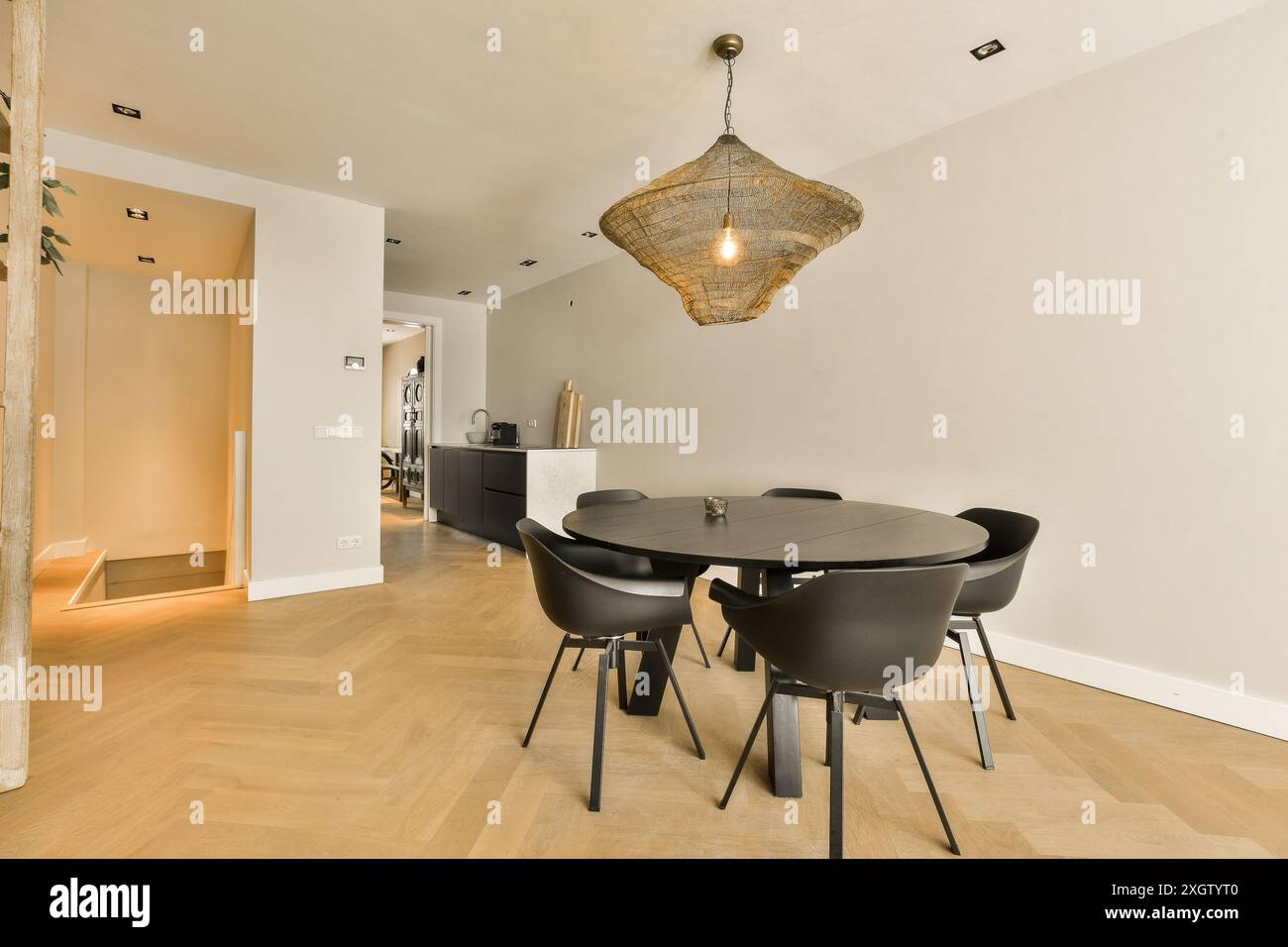 Moderner Speisesaal mit eleganten Möbeln und minimalistischer Einrichtung. Eine einzigartige Leuchte hängt über dem schlanken runden Tisch. Stockfoto