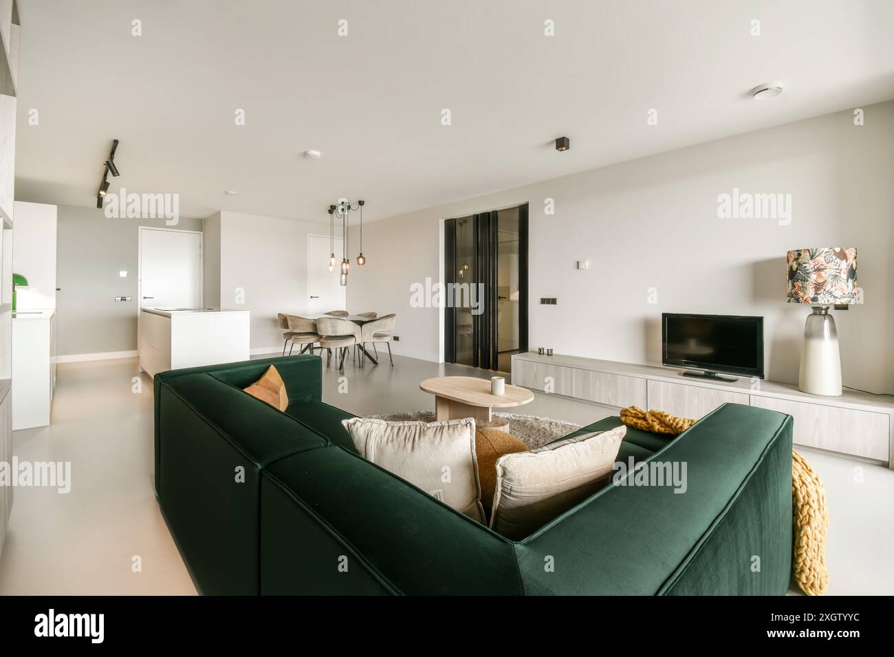 Helles, minimalistisches Wohnzimmer mit einem modernen grünen Sofa, offenem Grundriss und schicken Dekorationsakzenten. Stockfoto