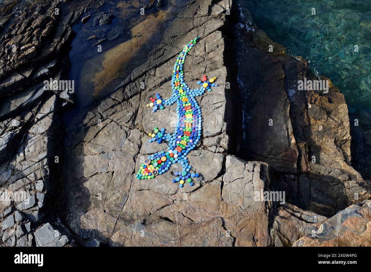 Gecko-Design auf Küstenfelsen aus Flaschenaufsätzen und Zigarettenanzündern, die an Stränden in Milina, South Pelion, Griechenland gesammelt wurden Stockfoto