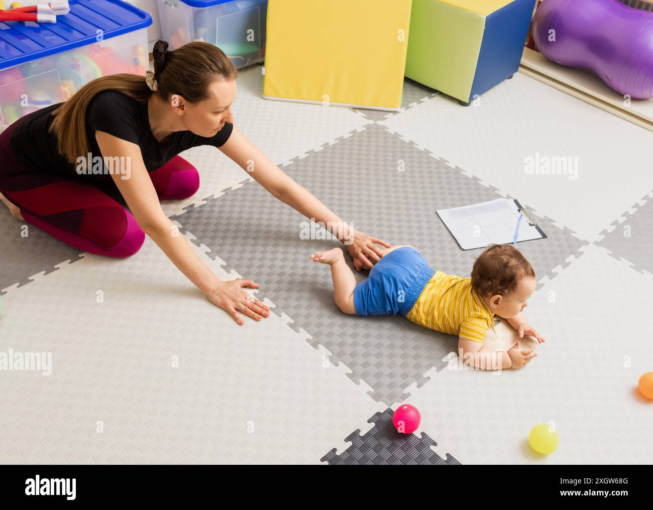 Physiotherapeut hilft Baby bei Krabbelübungen während der Rehabilitationssitzung. Frühzeitige Intervention bei Genesungsbewegungen und Koordinationsstörungen Stockfoto