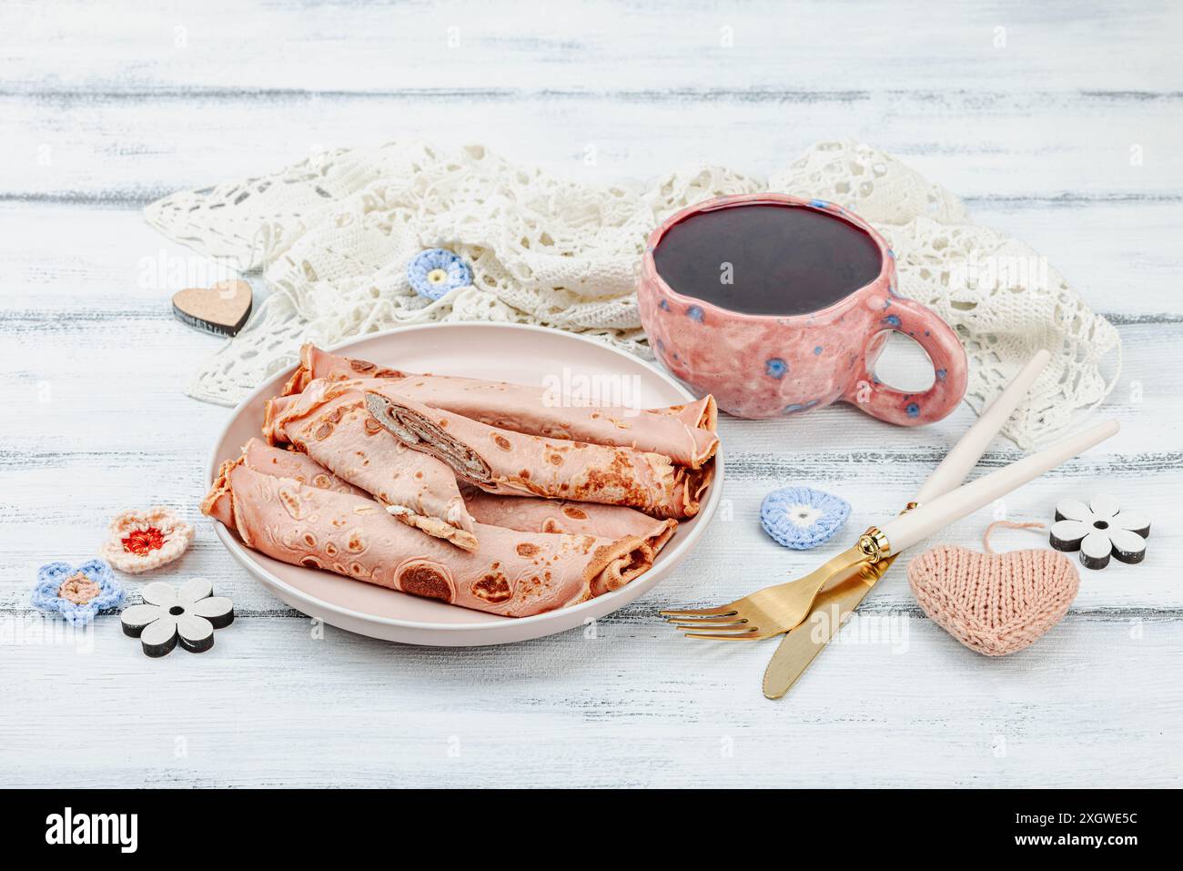 Eine Tasse duftenden Hibiskus-Tee und dünne Pfannkuchen mit Sahne. Gute Stimmung, gemütlicher Wohnkomfort. Weißer hölzerner Hintergrund, Kopierraum Stockfoto