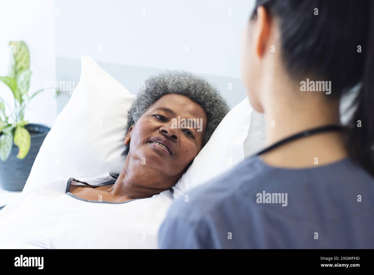 Eine ältere afroamerikanische Frau liegt in einem Krankenhausbett mit Kopierraum. Eine Krankenschwester sorgt für Pflege und hebt die mitfühlende Natur der Gesundheitsversorgung hervor. Stockfoto