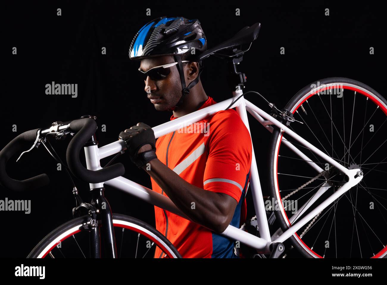 Afroamerikaner hält ein Rennrad auf schwarzem Hintergrund, mit Kopierraum. Er trägt Fahrradausrüstung und ist bereit für ein Rennen oder Training. Stockfoto