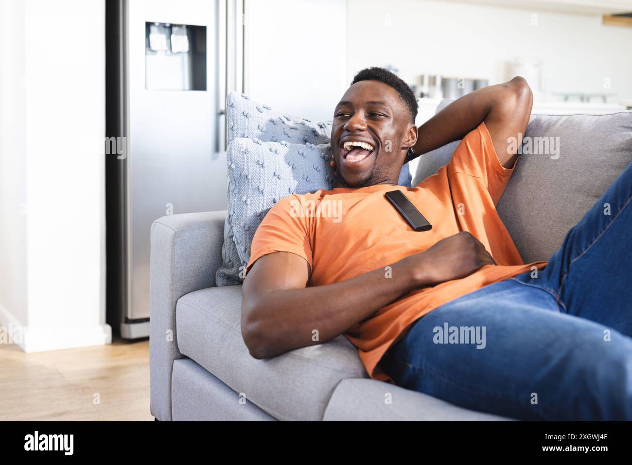 Glücklicher afroamerikanischer Mann, der sich auf dem Sofa lacht, fernsehen, Kopierraum sieht. Entspannung, Fernsehen, Technik, Unterhaltung, Freizeit, inländisch Stockfoto