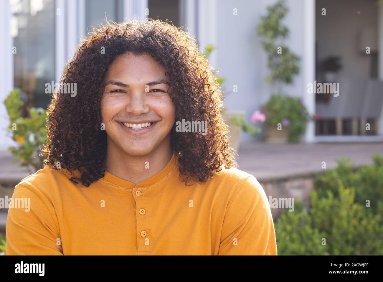 Junger Mann, der im Freien lächelt, unverfälscht. Sein fröhlicher Ausdruck hellt den Vorhof des Hauses auf. Stockfoto