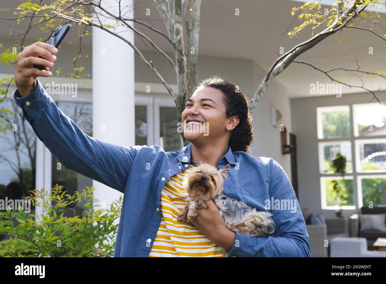 Ein junger birassischer Mann macht ein Selfie mit seinem Hund. Er fängt einen fröhlichen Moment in einem Garten ein. Stockfoto
