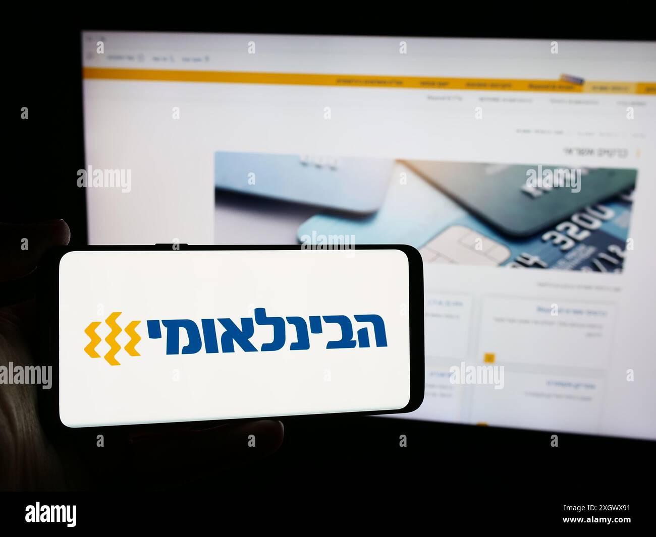 Person mit Smartphone und Logo der Firma First International Bank of Israel Ltd. (FIBI) vor der Website. Schwerpunkt auf dem Display des Telefons. Stockfoto