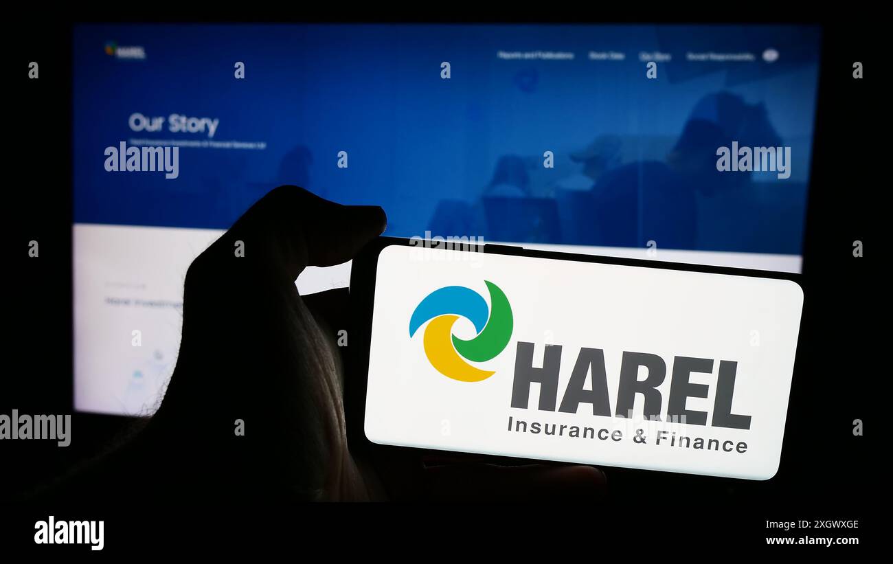 Person, die ein Mobiltelefon mit dem Logo von Harel Insurance Investments and Financial Services Ltd. Vor der Webseite hält. Schwerpunkt auf dem Display des Telefons. Stockfoto