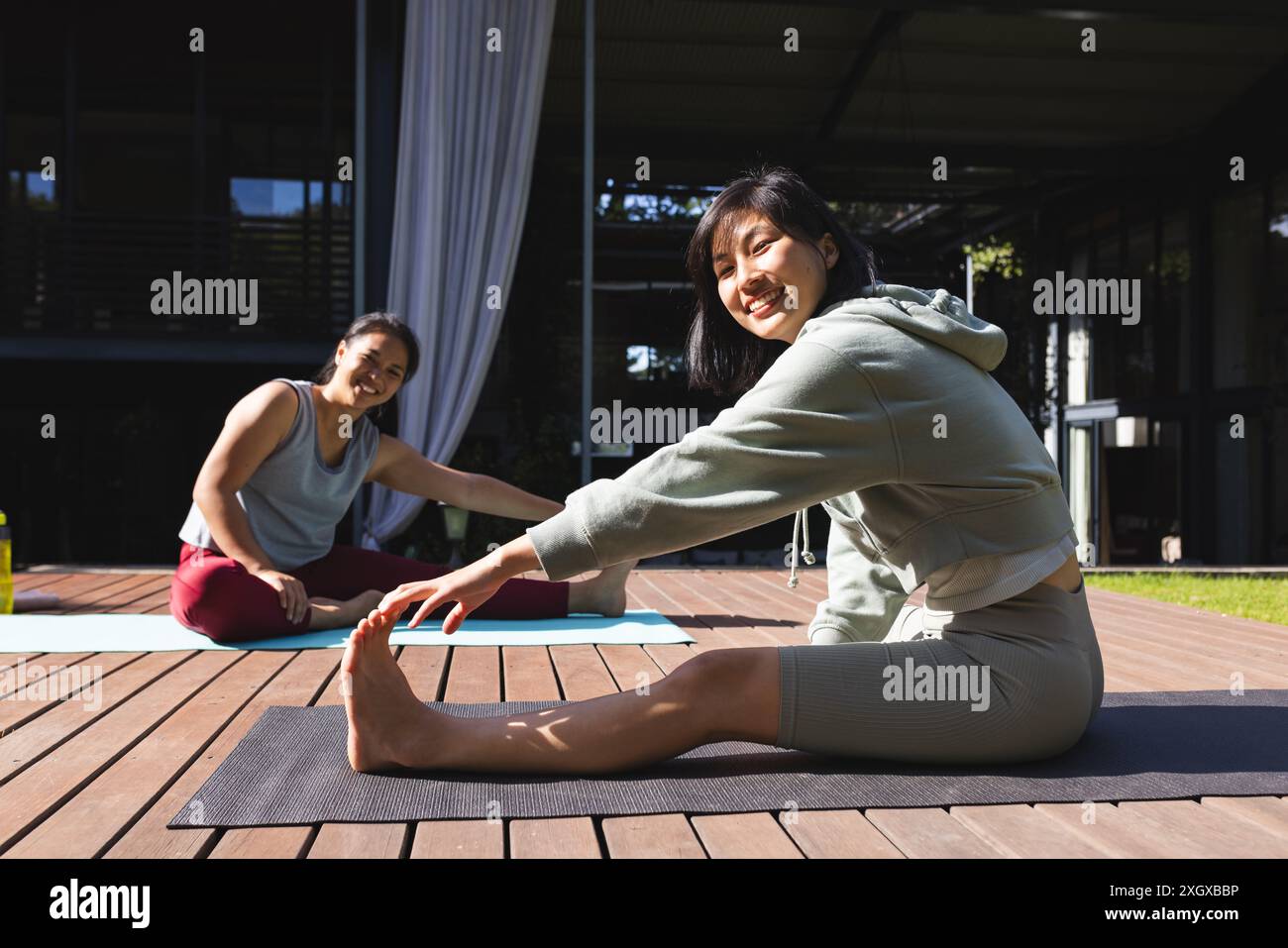Porträt glücklicher asiatischer Freundinnen, die zu Hause Yoga üben und sich im Garten dehnen. Fitness, Bewegung, häusliches Leben, Freundschaft, Aktivität und li Stockfoto