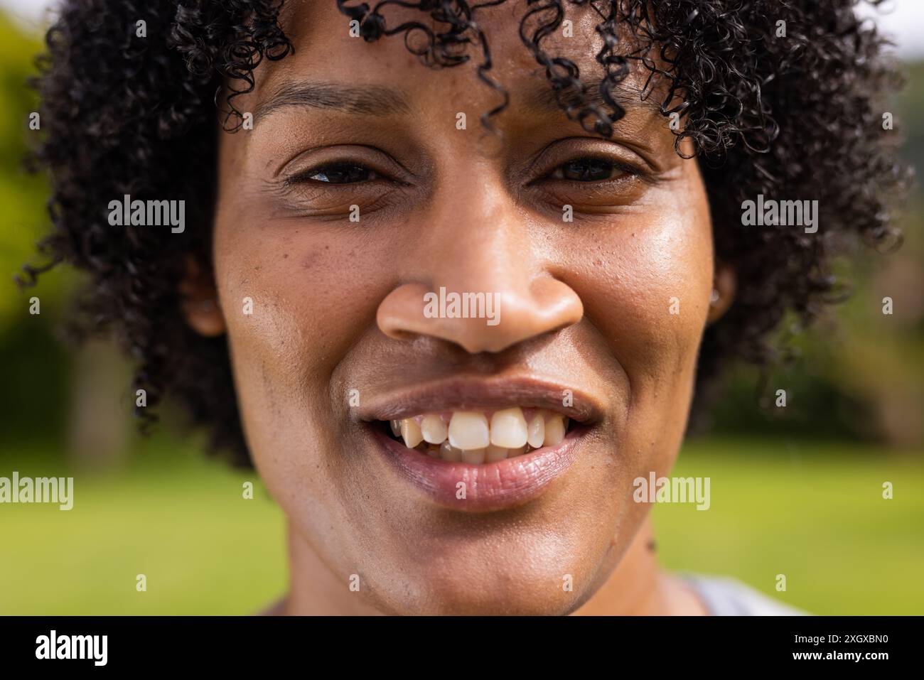Nahaufnahme einer jungen Frau, die draußen lächelt, mit unverändertem Kopierraum. Ihr fröhlicher Ausdruck erhellt die natürliche Umgebung um sie herum. Stockfoto