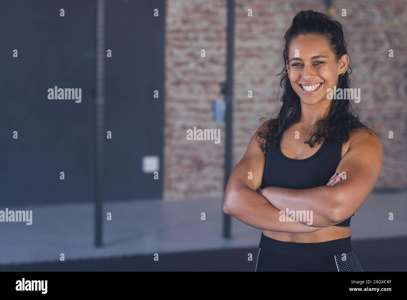 Eine starke und fitte junge Frau lächelt selbstbewusst im Fitnessstudio, mit unverändertem Kopierraum. Ihre sportliche Kleidung deutet auf ein Engagement für Fitness A hin Stockfoto