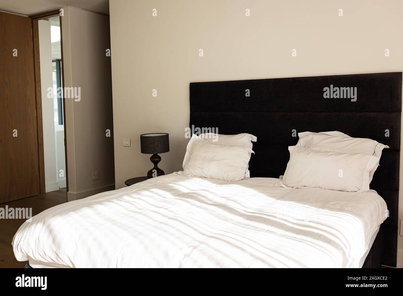 Ein modernes Schlafzimmer mit einem ordentlich gefertigten Bett und minimalistischer Einrichtung. Die Einfachheit des Zimmers vermittelt ein modernes Wohndesign mit Fokus auf Funktionalität Stockfoto