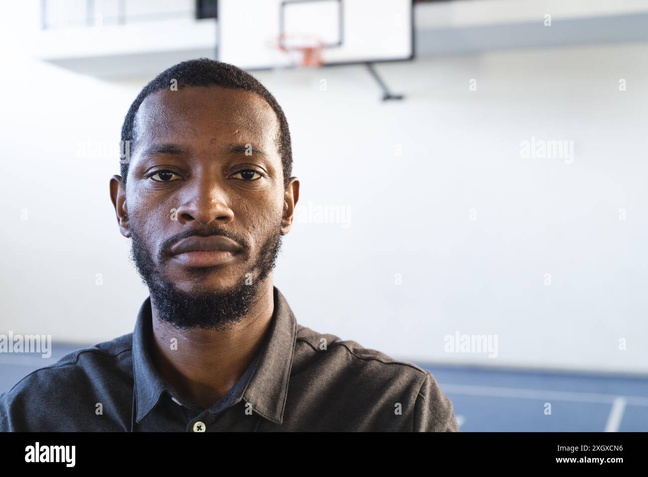 Ein afroamerikanischer Basketballtrainer in einem Fitnessstudio, der sowohl Sport als auch Lifestyle verkörpert, mit Kopierraum. Er scheint besinnlich mit einem Basketball zu sein Stockfoto