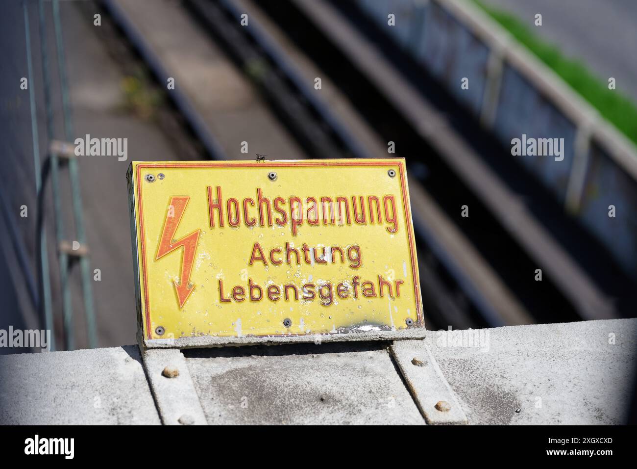 Gelbes Schild mit roter Aufschrift in deutscher Hochspannung Achtung Lebensgefahr auf einer Brücke über eine Eisenbahnstrecke Stockfoto