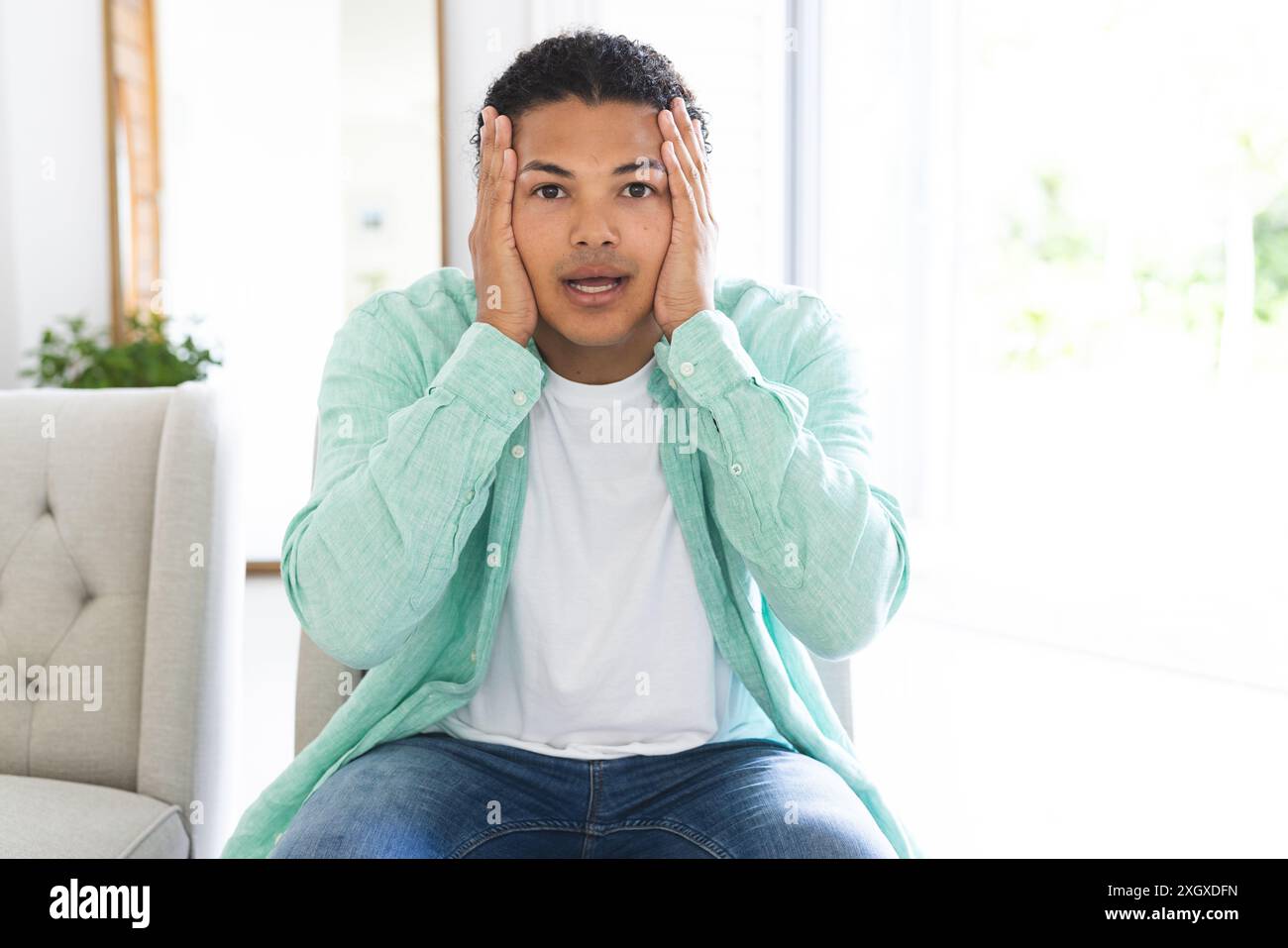 Ein junger birassischer Mann sieht überrascht aus während eines Videoanrufs zu Hause, mit Kopierraum. Sein Ausdruck deutet auf eine unerwartete Situation oder schockierende Nachrichten hin. Stockfoto