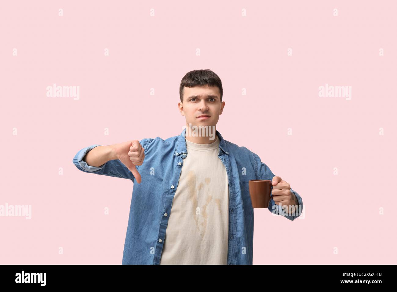 Junger Mann in schmutzigem T-Shirt mit einer Tasse Kaffee auf rosa Hintergrund Stockfoto