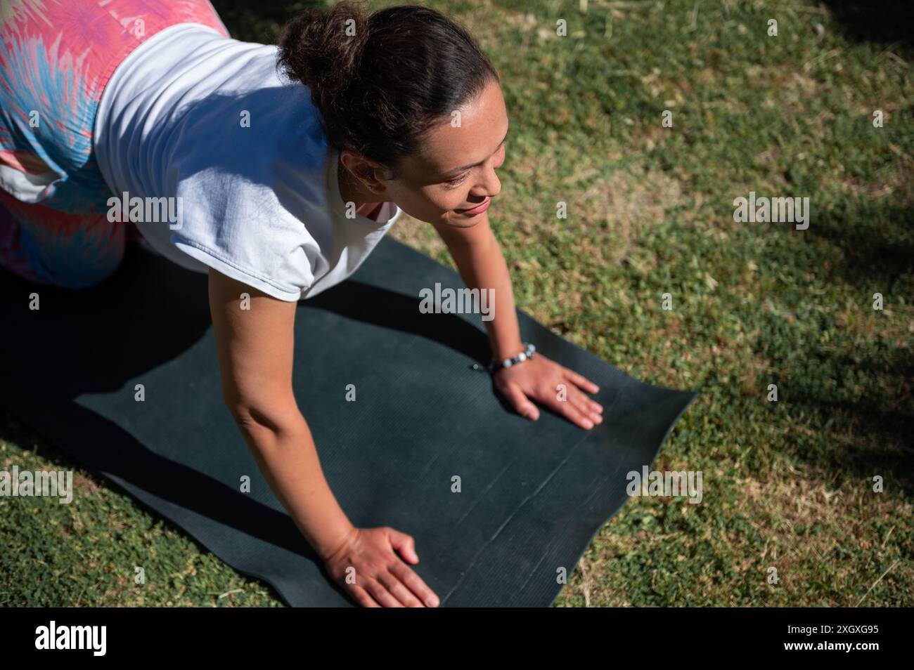 Eine Frau, die an einem sonnigen Tag im Freien Yoga praktiziert, eine Stretchposition auf einer Yogamatte auf dem Gras ausübt und die Vorteile körperlicher Übungen genießt Stockfoto