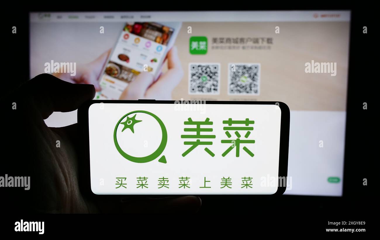 Person, die ein Handy mit dem Logo des chinesischen landwirtschaftlichen E-Commerce-Unternehmens Meicai vor der Business-Website hält. Schwerpunkt auf dem Display des Telefons. Stockfoto