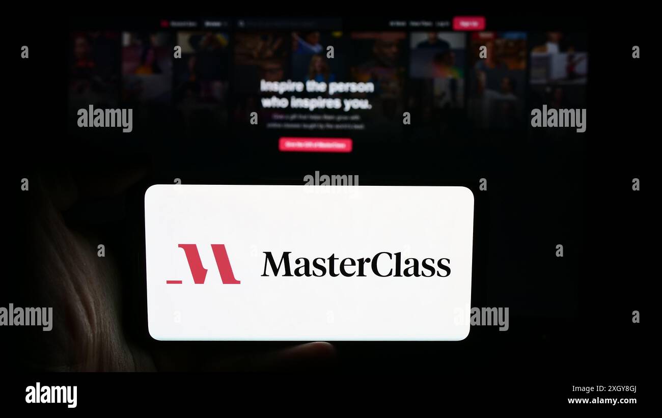 Person, die ein Mobiltelefon mit dem Logo des amerikanischen Bildungsunternehmens Yanka Industries Inc. (Masterclass) vor der Webseite hält. Schwerpunkt auf dem Display des Telefons. Stockfoto