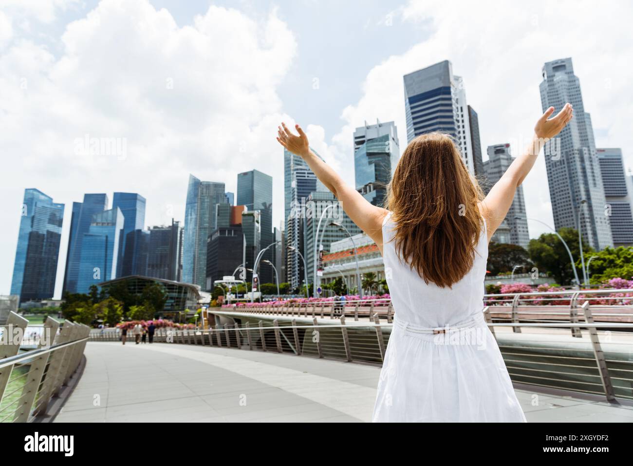 Junge Frau mit erhobenen Armen zum Himmel und genießt die Sonne und die wunderschöne Stadtlandschaft in der Innenstadt von Singapur Stockfoto