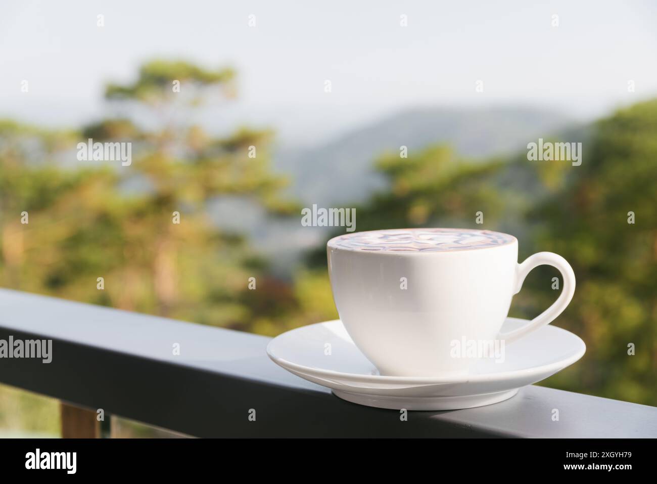 Tasse heißer Cappuccino-Kaffee auf Naturhintergrund. Frisches belebendes Getränk auf der Terrasse des Cafés. Stockfoto