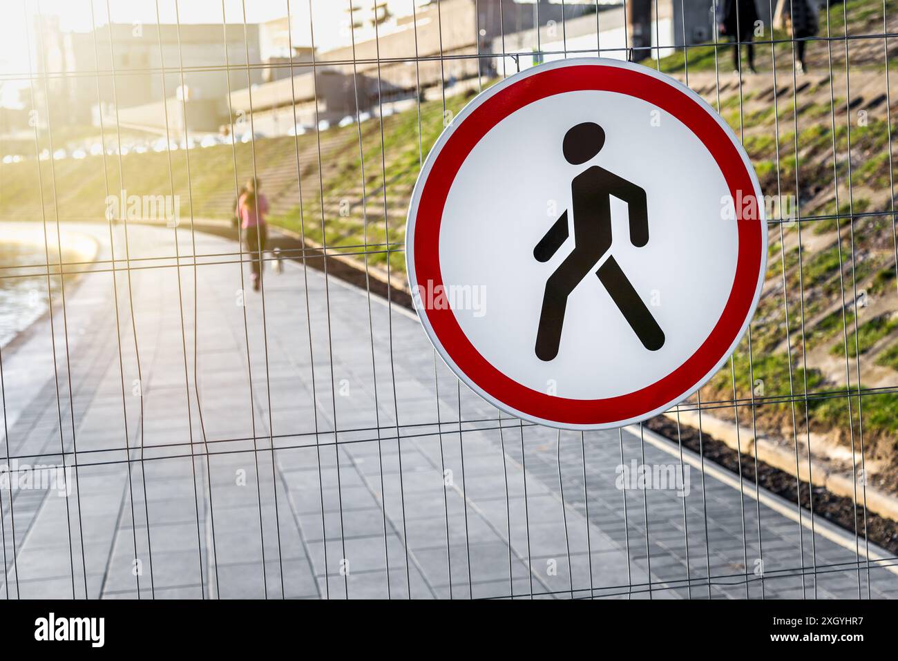 Kein Fußgängerschild hängt an Einem Metallzaundraht vor dem Hintergrund der Stadt Stockfoto