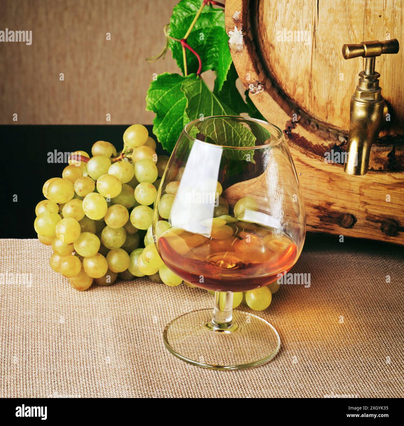 Ein Glas Brandy und ein Haufen reifer Trauben auf dem Tisch. Cognaczylinder ist rechts sichtbar. Umweltfreundliches Weinerzeugerprodukt. Klassisches alkoholisches Getränk. Stockfoto