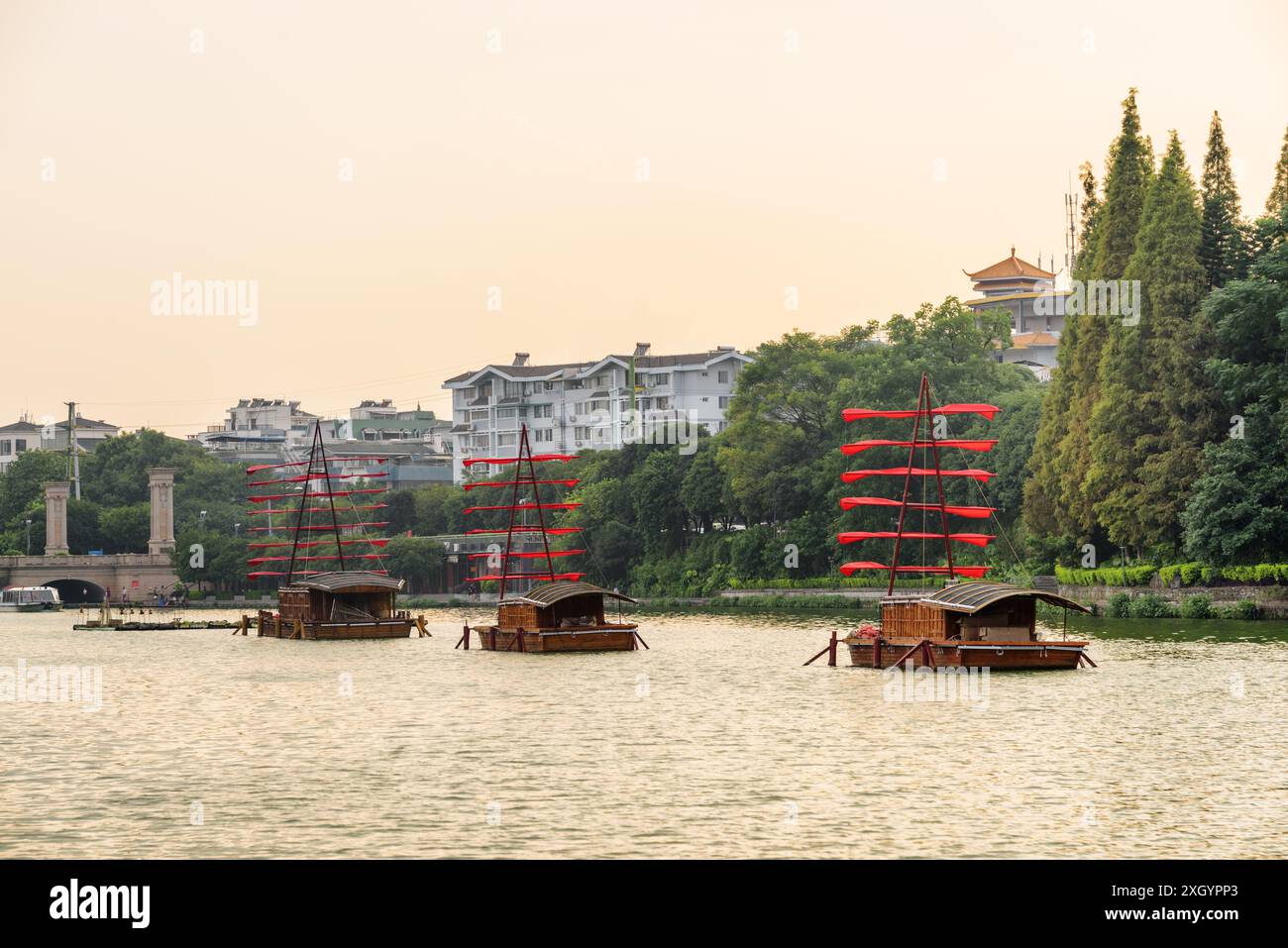 Malerische Holzschiffe, die mit roten Fahnen dekoriert sind und auf dem See in Guilin, China, parken. Wunderschöne Aussicht bei Sonnenuntergang. Stockfoto