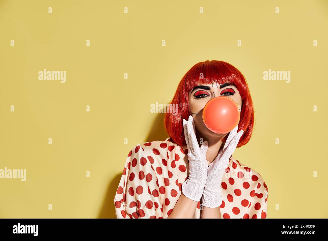 Eine hübsche rothaarige Frau mit Pop-Art-Make-up, bläst eine Blase auf gelbem Hintergrund. Stockfoto