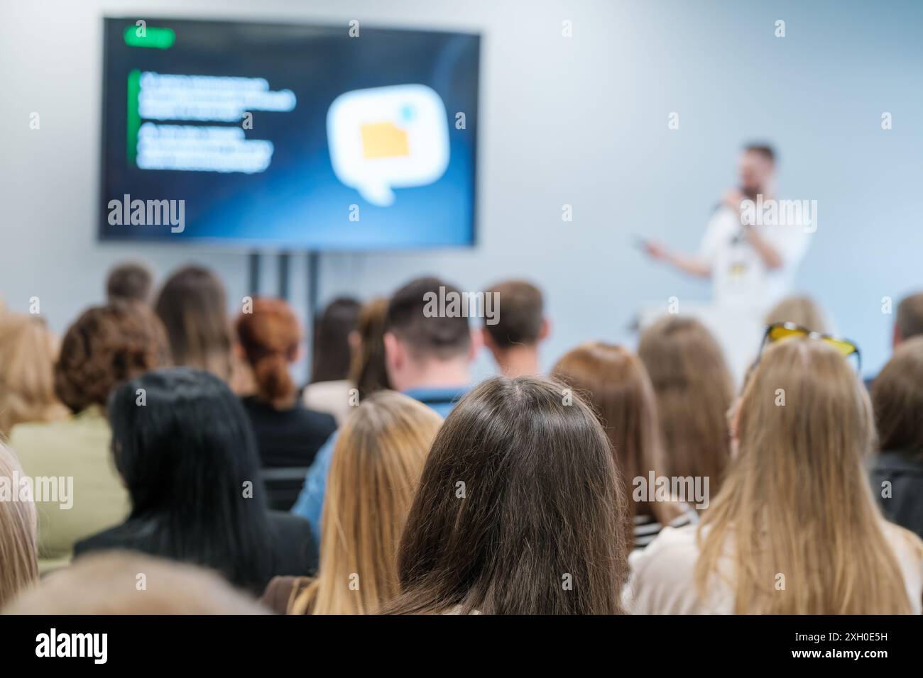 Verschiedene Zielgruppen in einer Geschäftskonferenz, die einem Sprecher mit einer Präsentation auf einem Bildschirm zuhören. Stockfoto