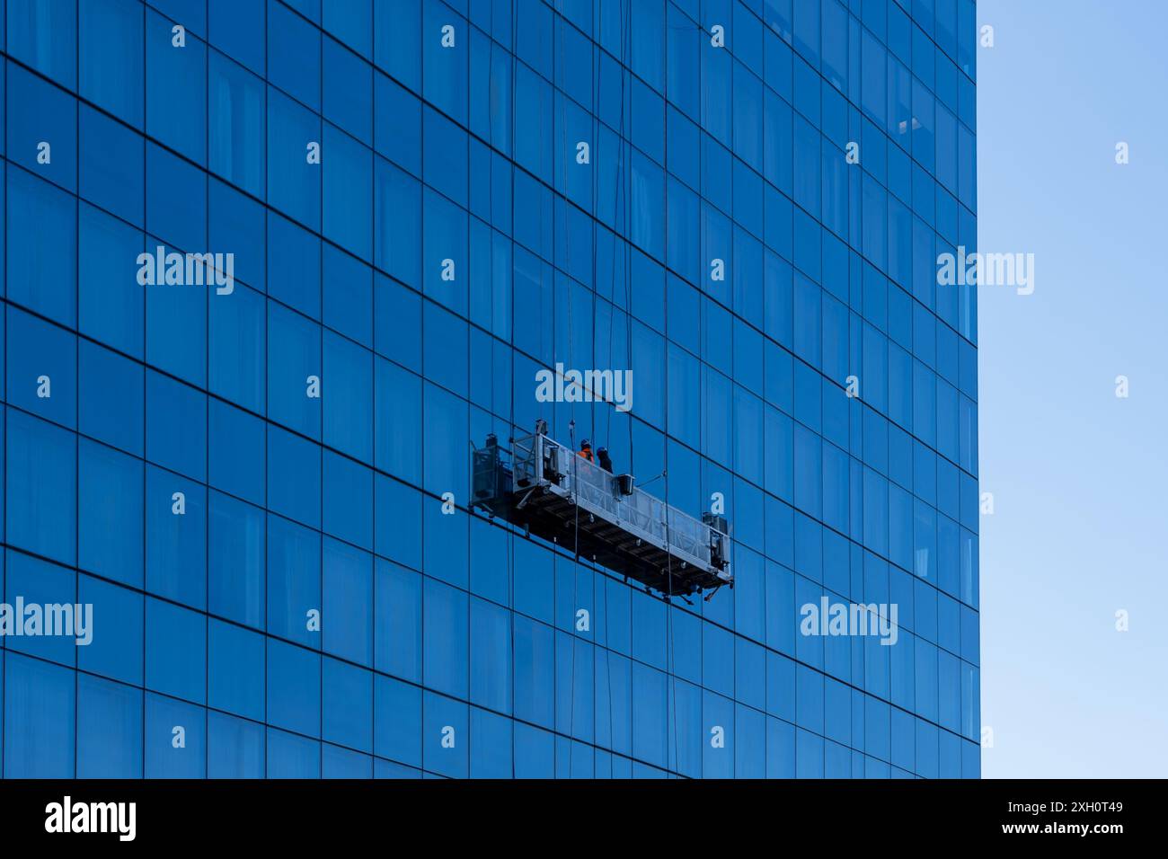 Buffalo, New York, USA - 8. Dezember 2023: Zwei Fensterreiniger in einer aufgehängten Plattform reinigen die Glasvorhangfassade eines Bürohochhauses Stockfoto