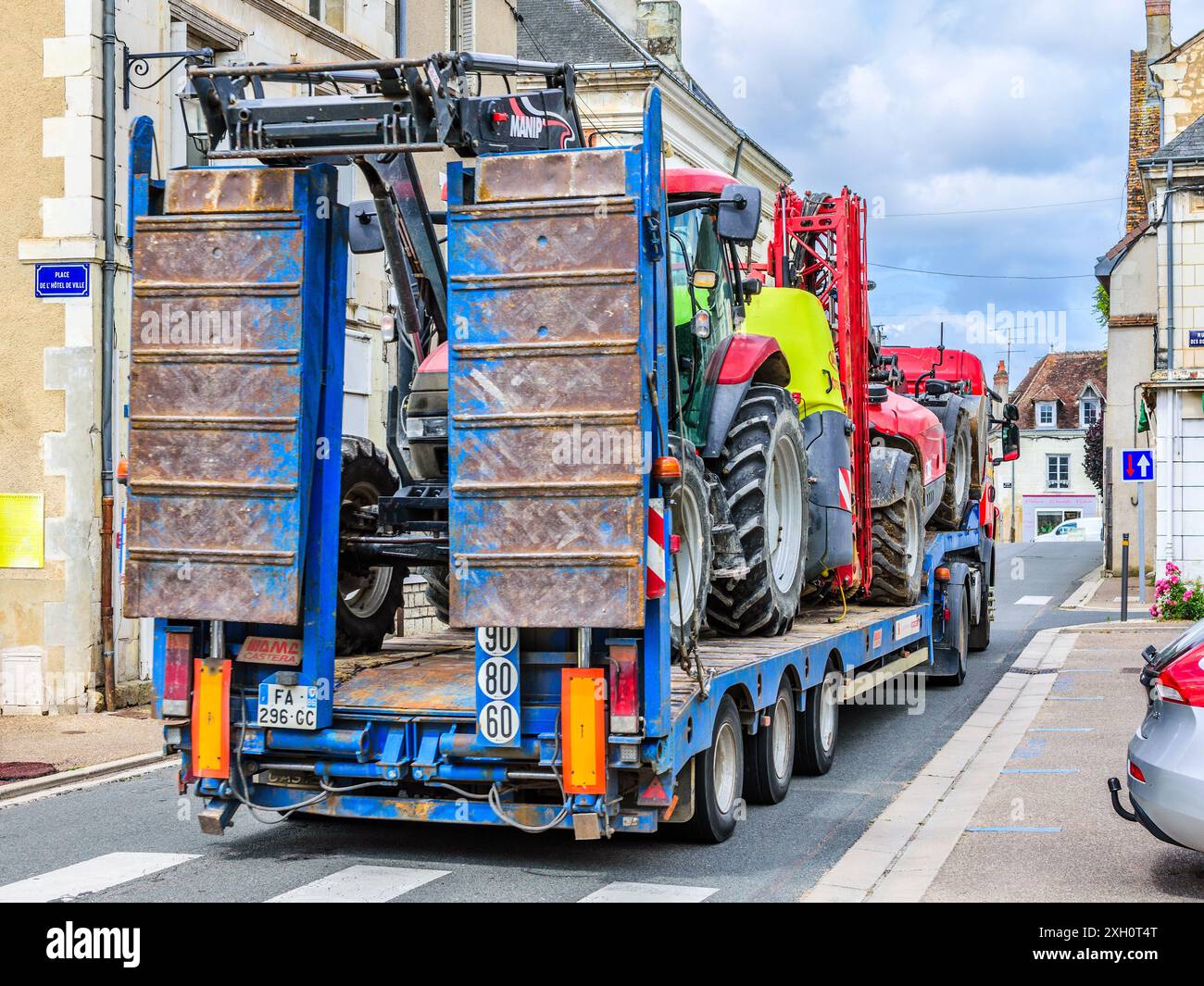 Landwirtschaftlicher Traktor auf einem langen Tieflader, der durch eine enge Straße in der Landstadt Preuilly-sur-Claise, Indre-et-Loire (37), Frankreich fährt. Stockfoto