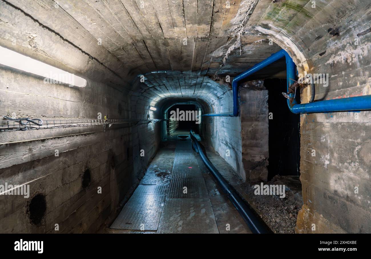 Industrieller Betontunnel mit blauen Rohren und elektrischen Leitungen, die ein Gefühl von Mysterium und Verlassenheit schaffen. Stockfoto