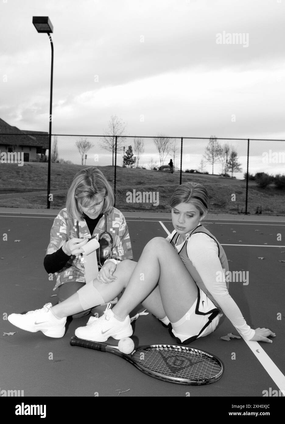 Weibliche Angestellte im Gesundheitswesen mit einem Stethoskop, das einen Verband um das Bein eines kaukasischen Teenagerinnen-Tennisspielers wickelt. USA Stockfoto