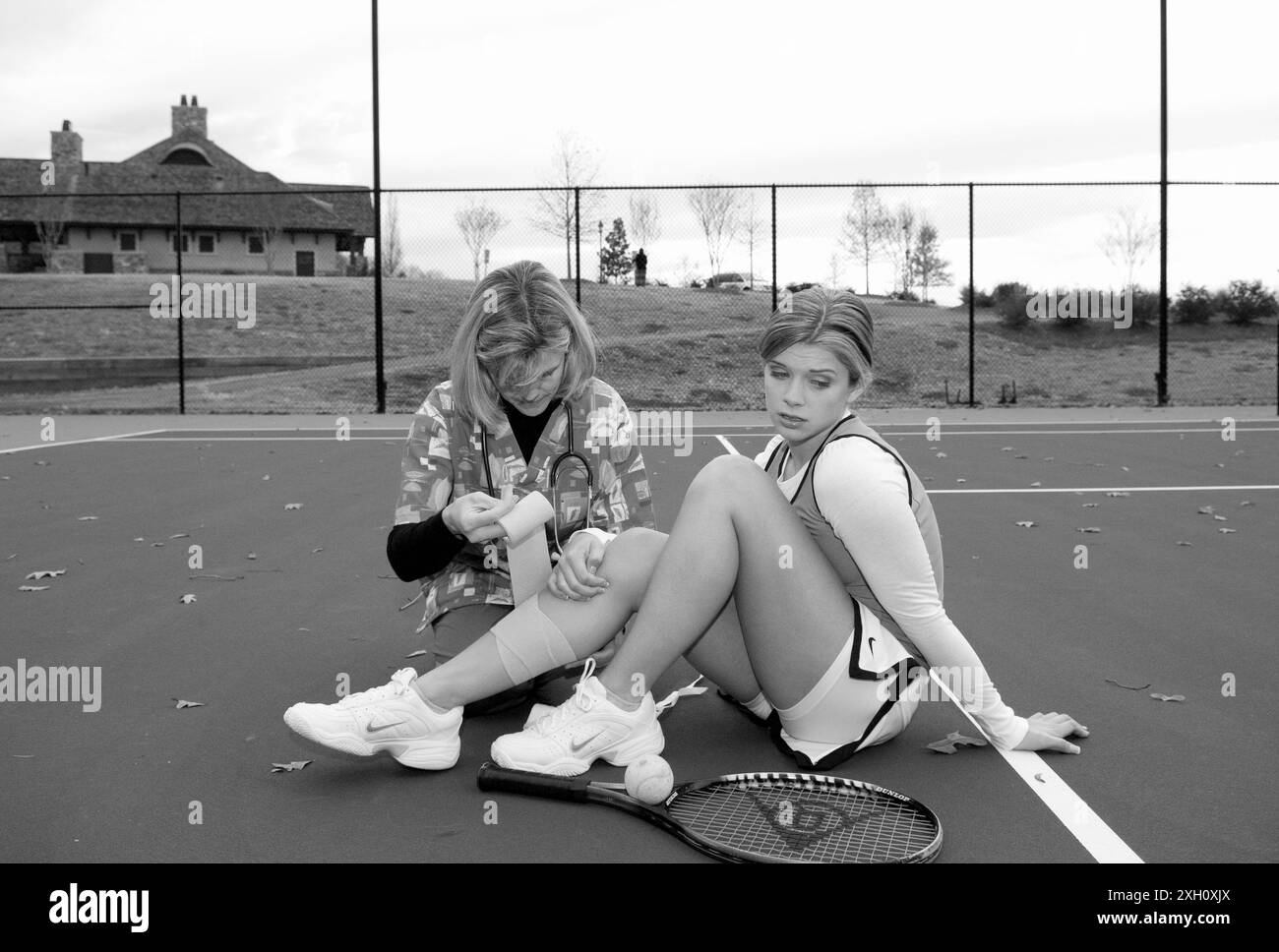 Stockfoto zeigt weibliche Gesundheitsberaterin mit Stethescope, die Bandage um das Bein eines kaukasischen Teenagermädchen-Tennisspielers von 15 bis 17 Jahren wickelt. Sh Stockfoto