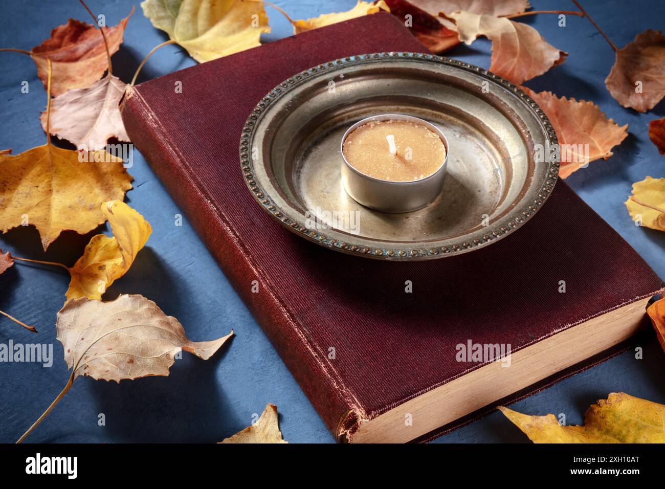 Herbstlesekonzept und altes Buch mit Kerze und Herbstblättern auf blauem Hintergrund Stockfoto